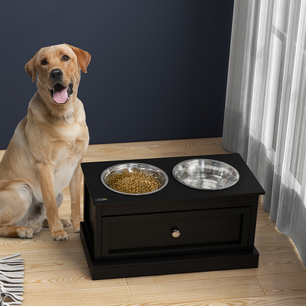 Happy dog beside black elevated pet feeder with food and water bowls, ideal for dog toys and accessories.